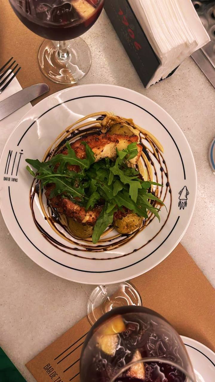 Prato gourmet com carnes douradas, rúcula verde e molho decorativo em prato branco com design elegante